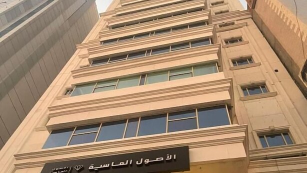 Un grand immeuble de couleur beige, doté de nombreuses fenêtres et d’une enseigne en arabe.