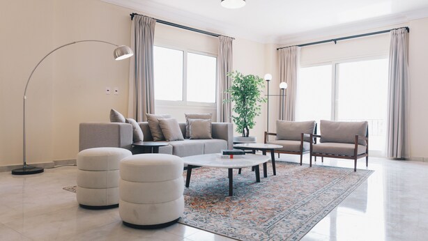 A modern living room with a sofa, armchairs, ottomans, a coffee table, and a floor lamp. - VIDA in Yasmeen - V302, VIDA Garden View Apartment (New Cairo City)