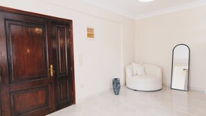 A room with a wooden door, a white sofa, a vase, and a mirror on the wall. - VIDA in Yasmeen - V302, VIDA Garden View Apartment (New Cairo City)