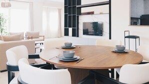 A modern dining area with a round wooden table, white chairs, and grey bowls on plates. - VIDA in Yasmeen - V302, VIDA Garden View Apartment (New Cairo City)