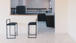A modern kitchen with a countertop and two bar stools. - VIDA in Yasmeen - V302, VIDA Garden View Apartment (New Cairo City)