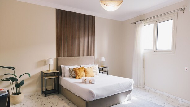 Une chambre avec un grand lit, deux tables de chevet, une plante en pot et une fenêtre avec des rideaux.