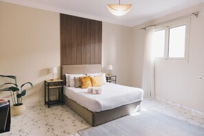 Un dormitorio con una cama grande, dos mesitas de noche, una planta en maceta y una ventana con cortinas.