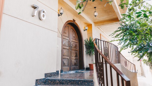 A building entrance with a wooden door, a staircase with a metal railing, and a potted plant.