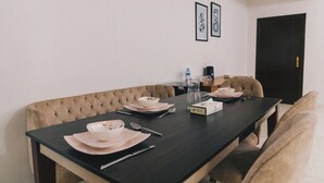 A dining room with a dark wooden table set for four, beige upholstered chairs, and a black door in the background. - The Seven Six Near Waterway 5A - 12, THE SEVEN SIX near WATERWAY 5A MALL By ELEGANT (New Cairo City)