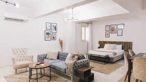 A modern living room with a sofa, armchair, coffee table, and a bed with a wooden headboard. - The Seven Six Near Waterway 5A - 12, THE SEVEN SIX near WATERWAY 5A MALL By ELEGANT (New Cairo City)
