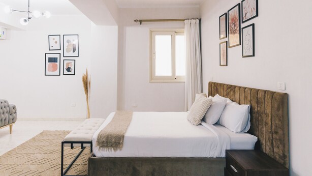 A modern bedroom with a bed, bedside table, and a window with curtains. - The Seven Six Near Waterway 5A - 12, THE SEVEN SIX near WATERWAY 5A MALL By ELEGANT (New Cairo City)