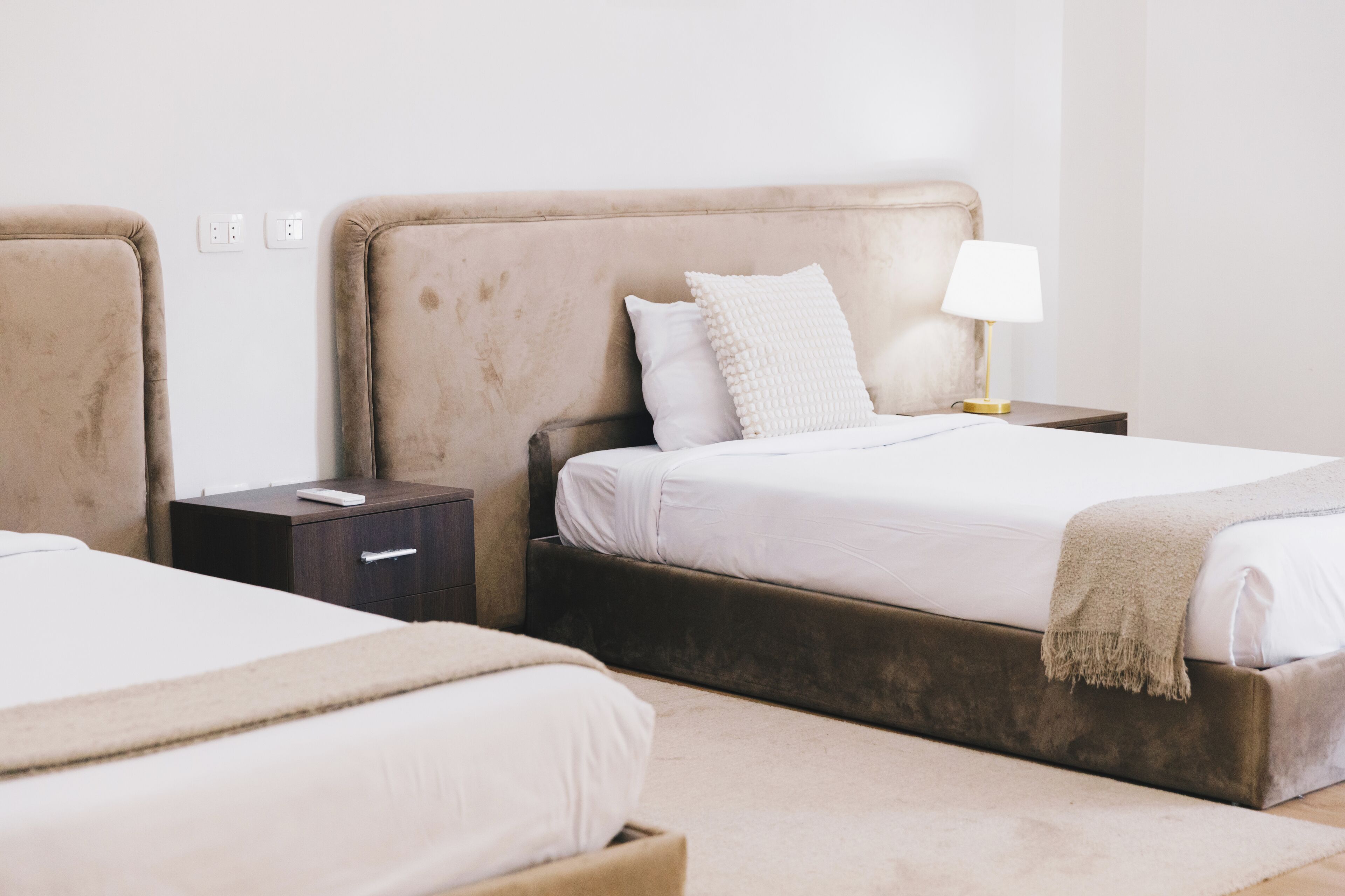 Una habitación de hotel con dos camas, una mesita de noche con lámpara y un mueble auxiliar con cajón.