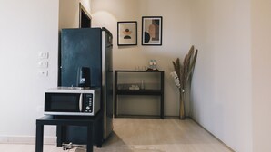 Une cuisine compacte équipée d’un four à micro-ondes, d’un réfrigérateur noir et d’une petite table. Deux tableaux encadrés ornent le mur, et un vase contient des plantes séchées.
