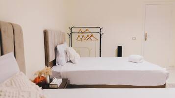 Una cama bien hecha con ropa de cama blanca, una mesita de noche con una lámpara y un perchero metálico con perchas.