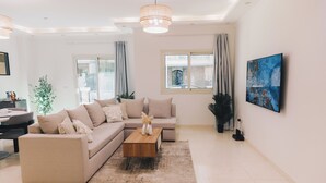 A modern living room with a beige sectional sofa, a wooden coffee table, and a large abstract painting on the wall. - VIOLA Near Waterway - 11, VIOLA New Studio - Higher Floor (New Cairo City)