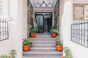 Un escalier bordé de chaque côté de jardinières, menant à une porte surmontée d’un portail décoratif.