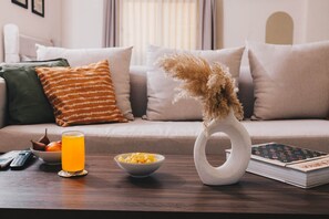 A living room with a sofa, a coffee table, a bowl of cereal, a glass of orange juice, a remote control, and a book.