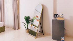 A room with a standing mirror, a small refrigerator, a potted plant, and a wall with a poster.