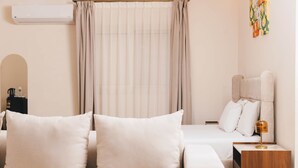 A hotel room with a bed, a bedside table with a lamp, a window with curtains, and a wall-mounted air conditioner.
