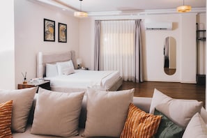 Une chambre d’hôtel avec un lit, une table de chevet, une lampe, un miroir et une fenêtre avec des rideaux.