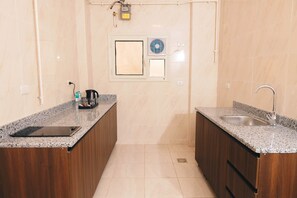 A compact kitchen with granite countertops, wooden cabinets, a built-in sink, and a window with blinds. - VIOLA Near Waterway - 32, VIOLA New Studio - Higher Floor (New Cairo City)