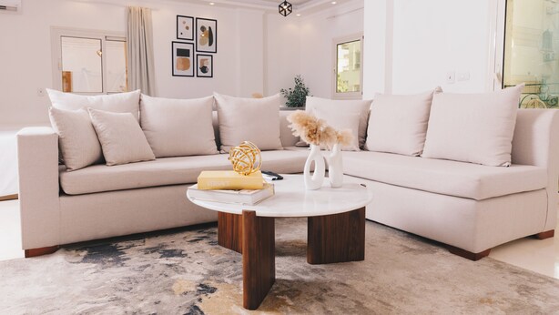 Een moderne woonkamer met een beige bank, een salontafel en decoratieve objecten.
