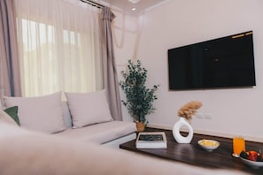 Una sala de estar moderna con un sofá, un televisor de pantalla plana, una planta en maceta, un jarrón con flores secas, un bol de palomitas de maíz y un vaso de jugo de naranja.