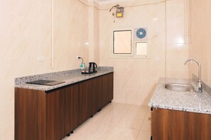 A modern kitchen with a granite countertop, wooden cabinets, a built-in sink, and a window with blinds. - VIOLA Near Waterway - 32, VIOLA New Studio - Higher Floor (New Cairo City)