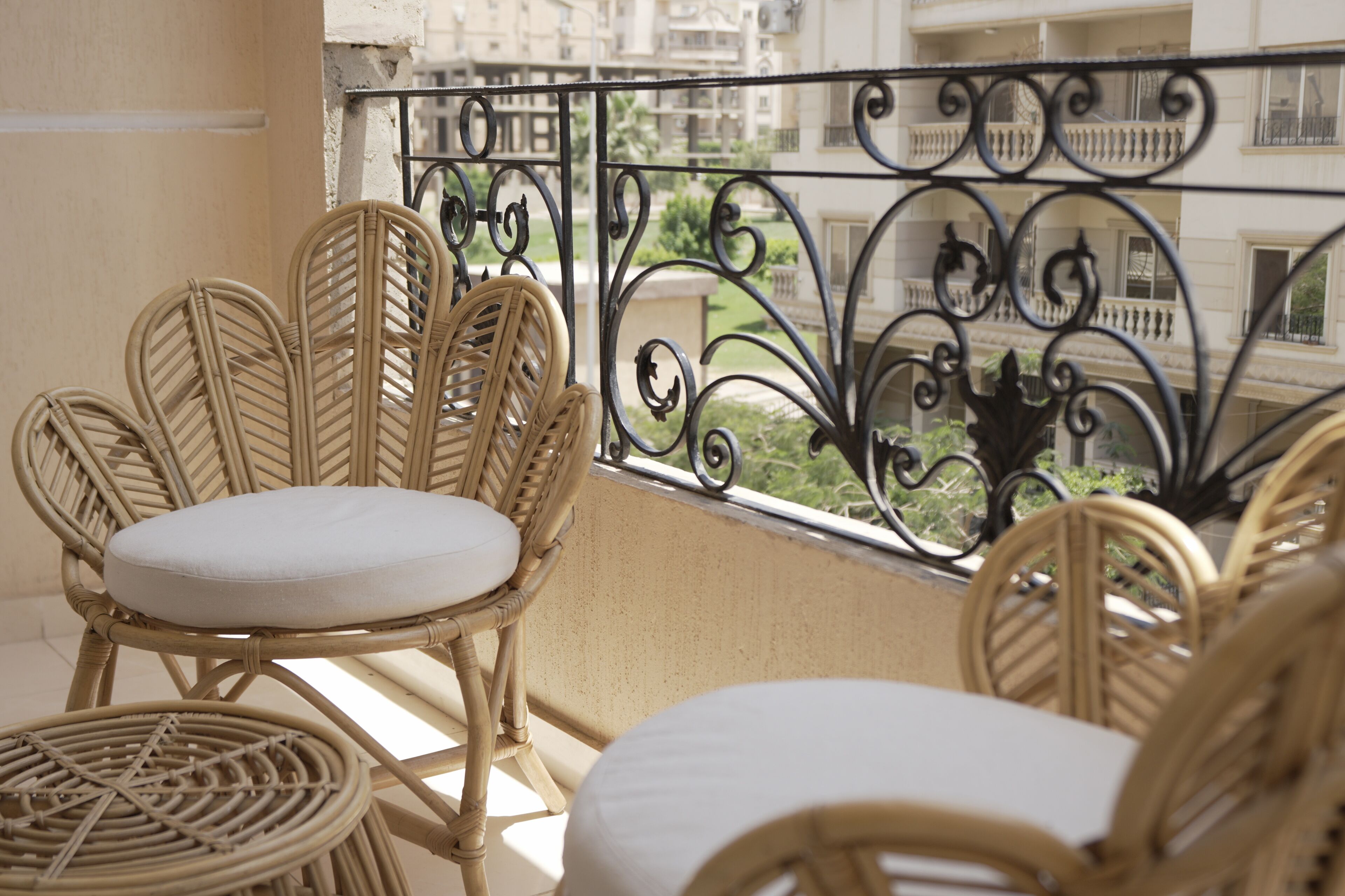 Wicker chairs with white cushions on a balcony with a wrought iron railing.