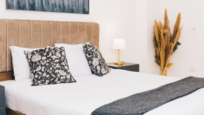 A neatly made bed with white and black floral pillows, a beige headboard, a bedside lamp, and a vase with dried plants. - VIOLA Near Waterway - 02, VIOLA New Studio - Ground Floor (New Cairo City)