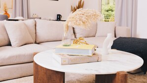 A living room with a sofa, a coffee table with books and a vase, and a view of the outdoors through a window. - VIOLA Near Waterway - 02, VIOLA New Studio - Ground Floor (New Cairo City)