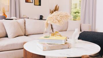 A living room with a sofa, a coffee table with books and a vase, and a view of the outdoors through a window.