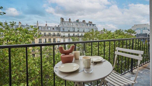 A balcony with a table set for two, a chair, and a view of a historic building. - Amazing Apartment Le Marais Center of Paris (Paris)