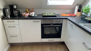 A modern kitchen with white cabinets, a built-in oven, a coffee maker, and various fruits and vegetables on the counter. - Meeresbrise 2 Top location with terrace. Pet friendly! (Tönning)