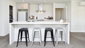 A modern kitchen with a central island, four stools, and a built-in oven. - Woodend Getaway, Modern 3-Bedroom, 2-Bathroom Home,  (Woodend)