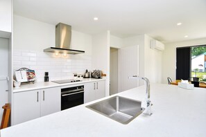 A modern kitchen with white cabinetry, a stainless steel sink, and a built-in oven. - Charming 3-Bedroom, 2-Bathroom Home (Woodend)