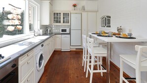 A modern kitchen with white cabinetry, a built-in washing machine, a dining area with white chairs, and a view of the outdoors. - The Seahorse Bungalow Park Sollasi (Noordwijkerhout)