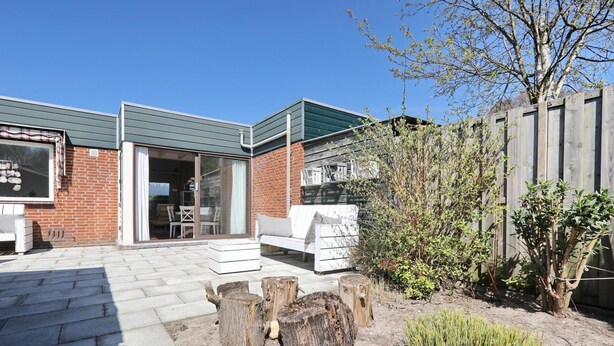 A patio area with a brick wall, a white outdoor sofa, and a wooden fence. - The Seahorse Bungalow Park Sollasi (Noordwijkerhout)