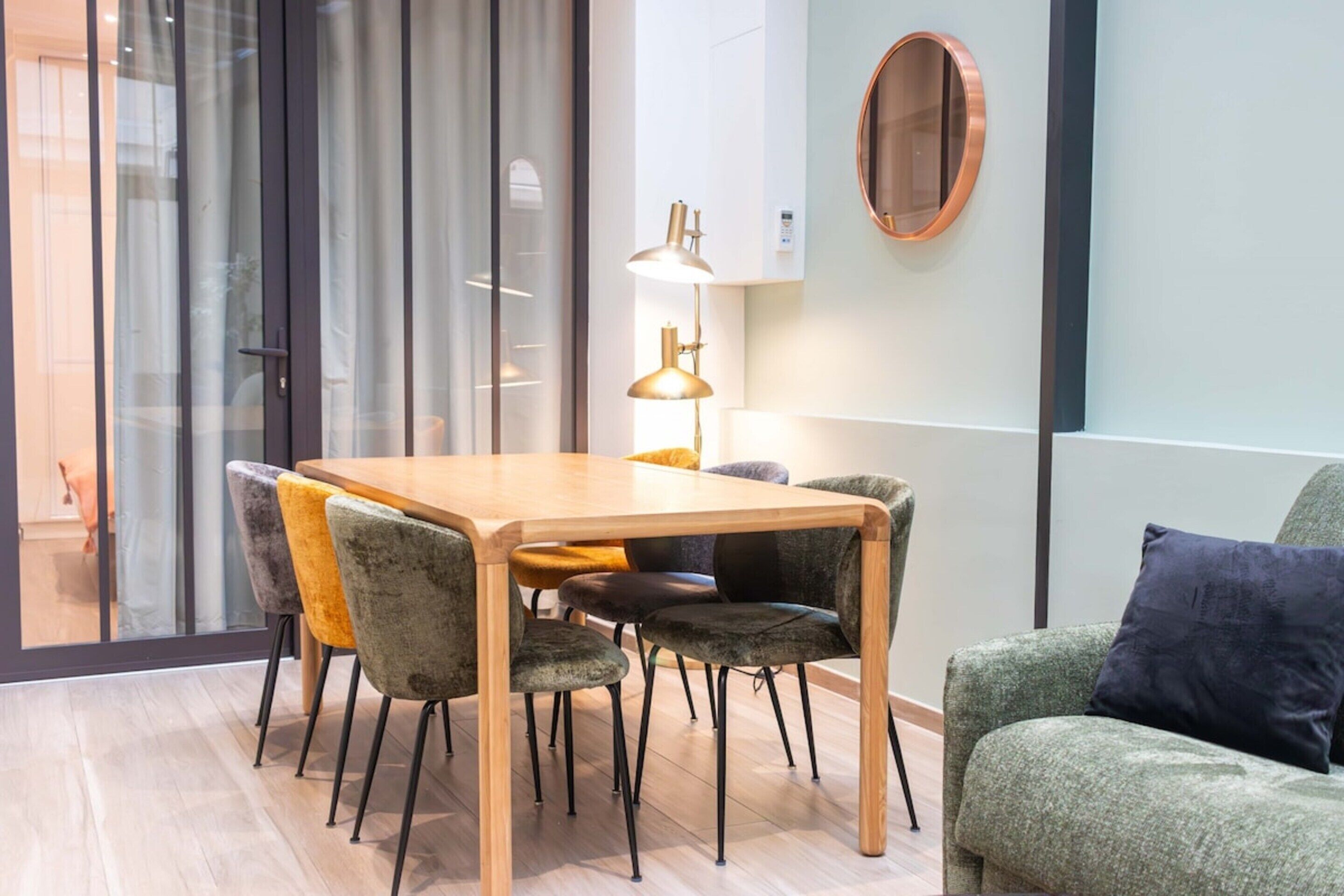 A modern dining area with a wooden table and chairs, a lamp, and a green sofa.