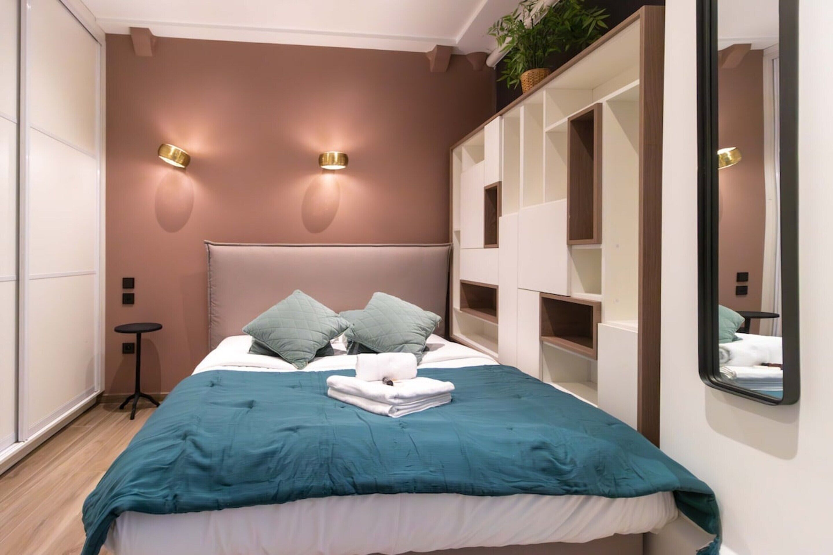 Un dormitorio moderno con una cama grande, dos luces fijadas a la pared, un espejo y almacenamiento empotrado.