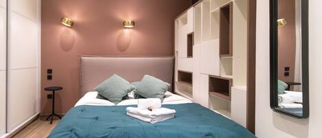 Un dormitorio moderno con una cama grande, dos luces fijadas a la pared, un espejo y almacenamiento empotrado.