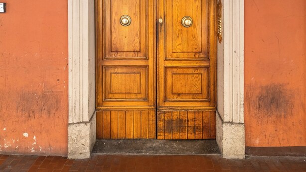 Una porta doppia in legno con cornice bianca, un cartello con il numero 56 sopra e un'apertura finestrata sopra la porta.