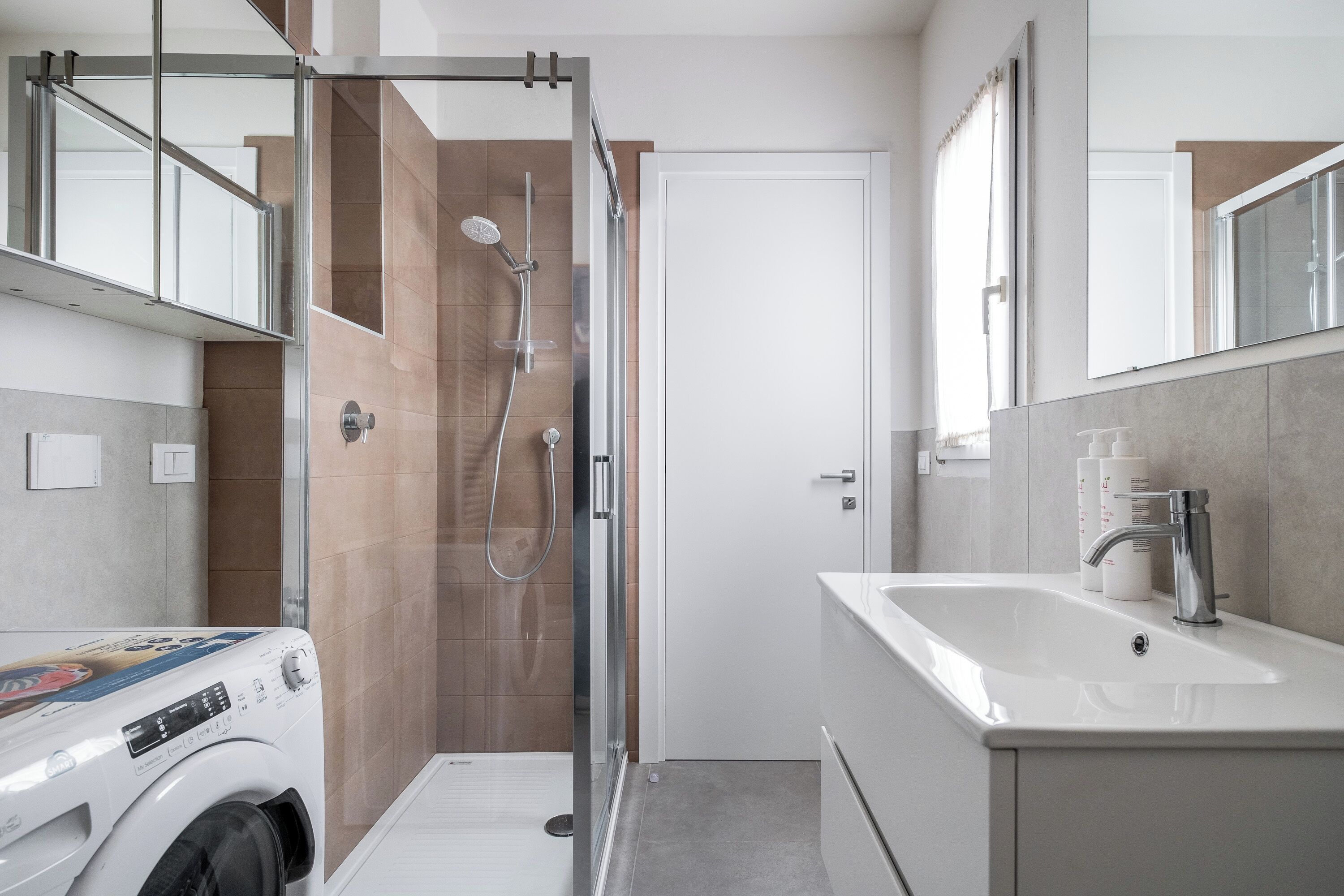 Un baño moderno con ducha de vidrio, lavadora integrada y un lavamanos grande con espejo arriba.