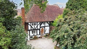 Una casa de estilo Tudor tradicional, con techo empinado, paredes blancas y entramado de madera negra, y un camino de entrada de grava.