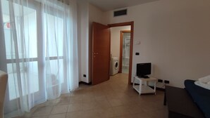 A room with a bed, a TV on a stand, a washing machine, and a door leading to another room. - Leopolda Suite (Florence)