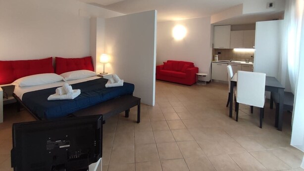 A hotel room with a bed, a desk, a red sofa, and a kitchenette. - Leopolda Suite (Florence)