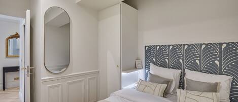A hotel room with a large bed, a bedside table, a mirror, and a decorative headboard.