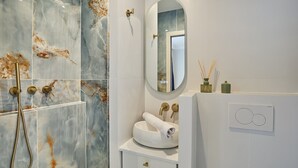 Un baño con pared de ducha de mármol, un espejo redondo, un lavamanos blanco con una toalla y un calentador de pared.