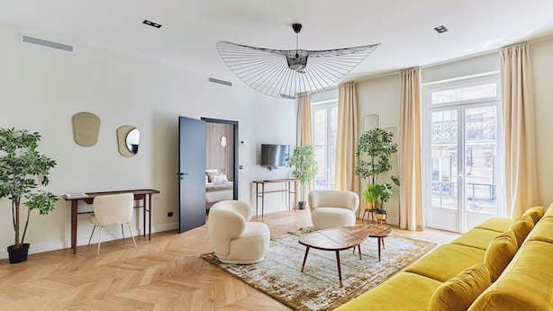 Ein modernes Wohnzimmer mit Fischgrätparkett, einem gelben Sofa, einem runden Couchtisch und einem Deckenventilator.