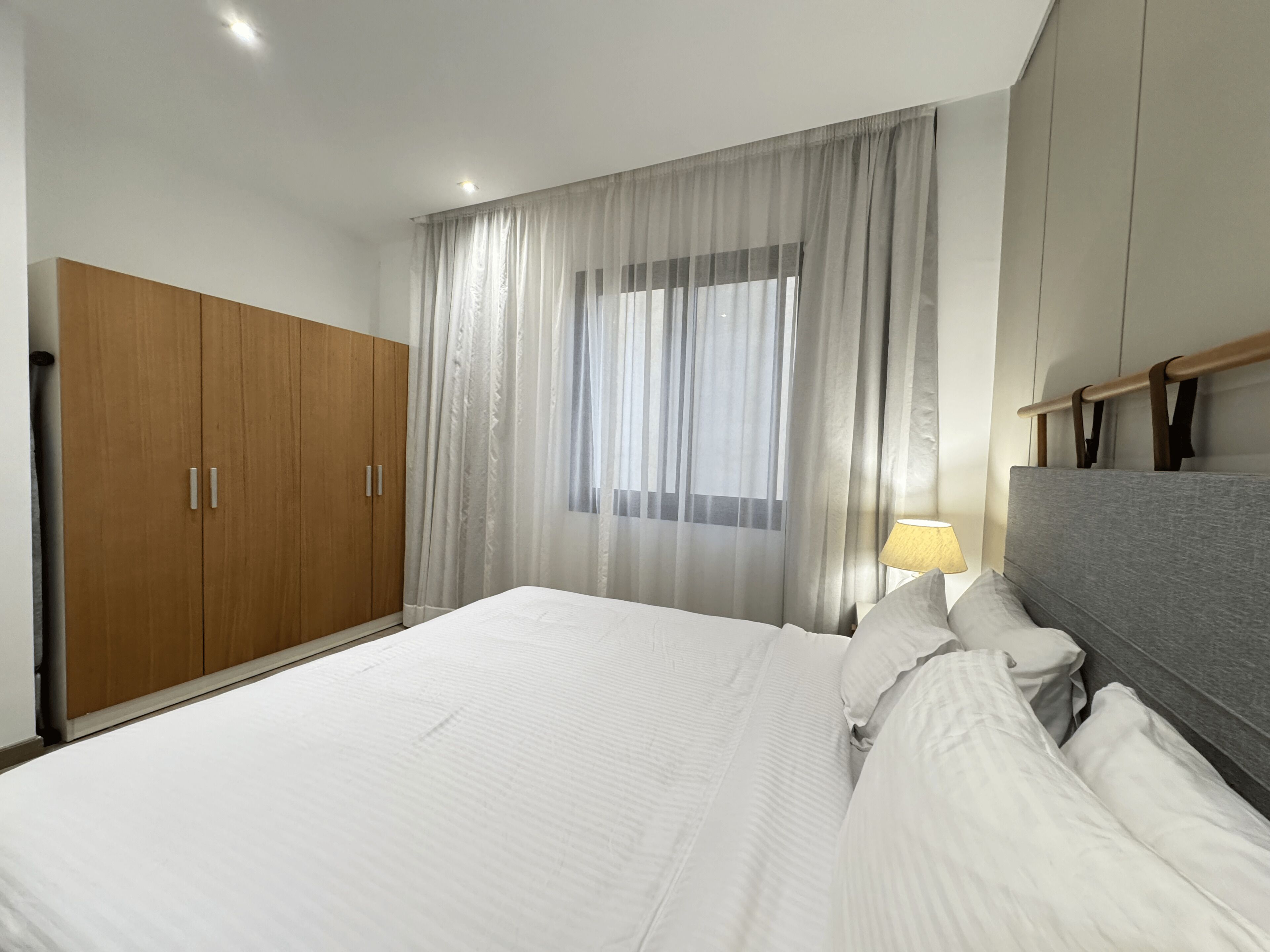 A bedroom with a large bed, wooden wardrobe, and a window with sheer curtains.