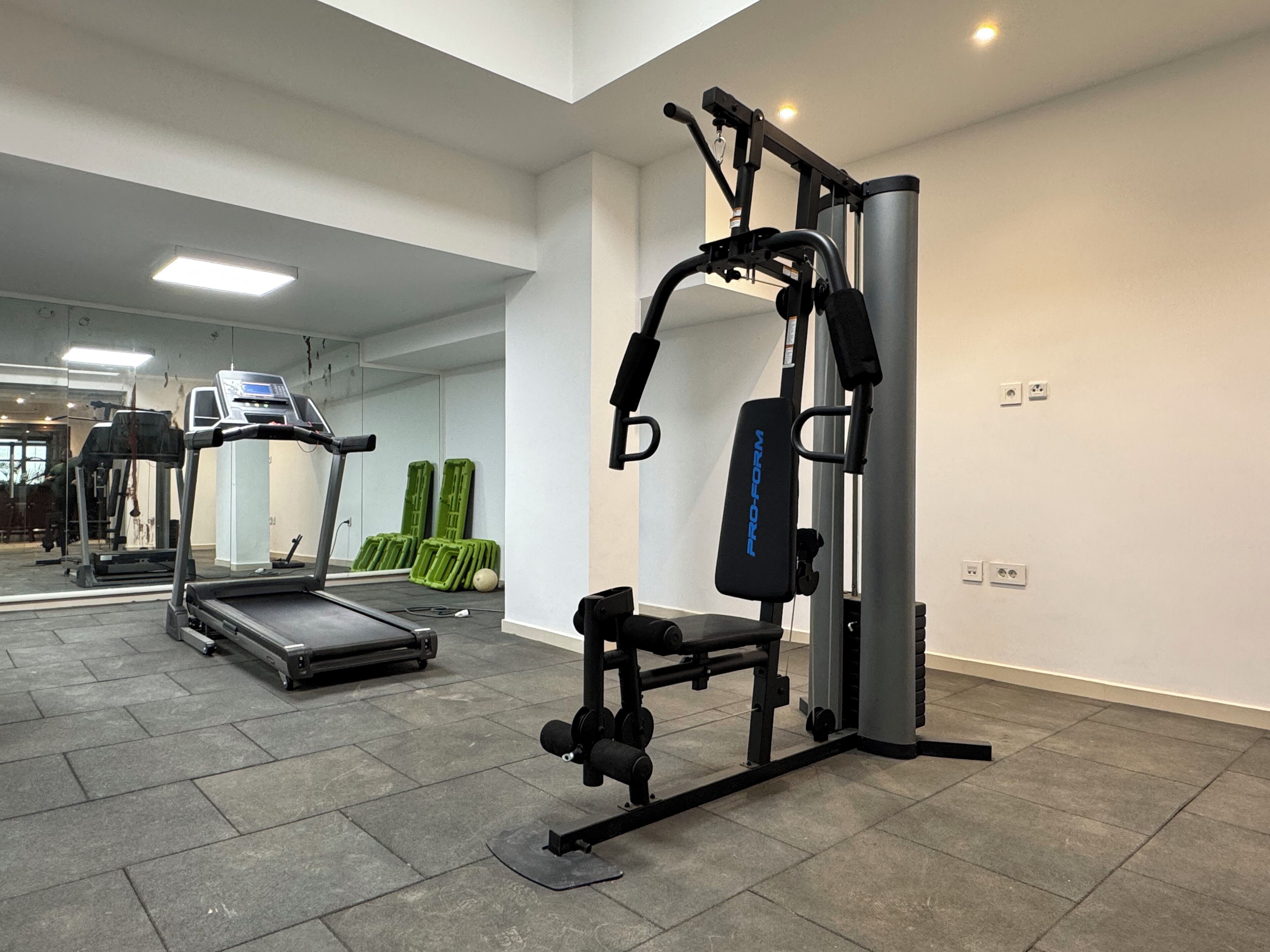 Ett gym med löpband, styrketräningsmaskin och gröna träningsmattor.