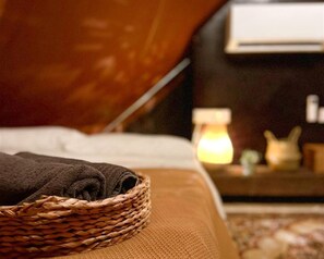 A neatly made bed with a dark towel and a woven basket on the side.