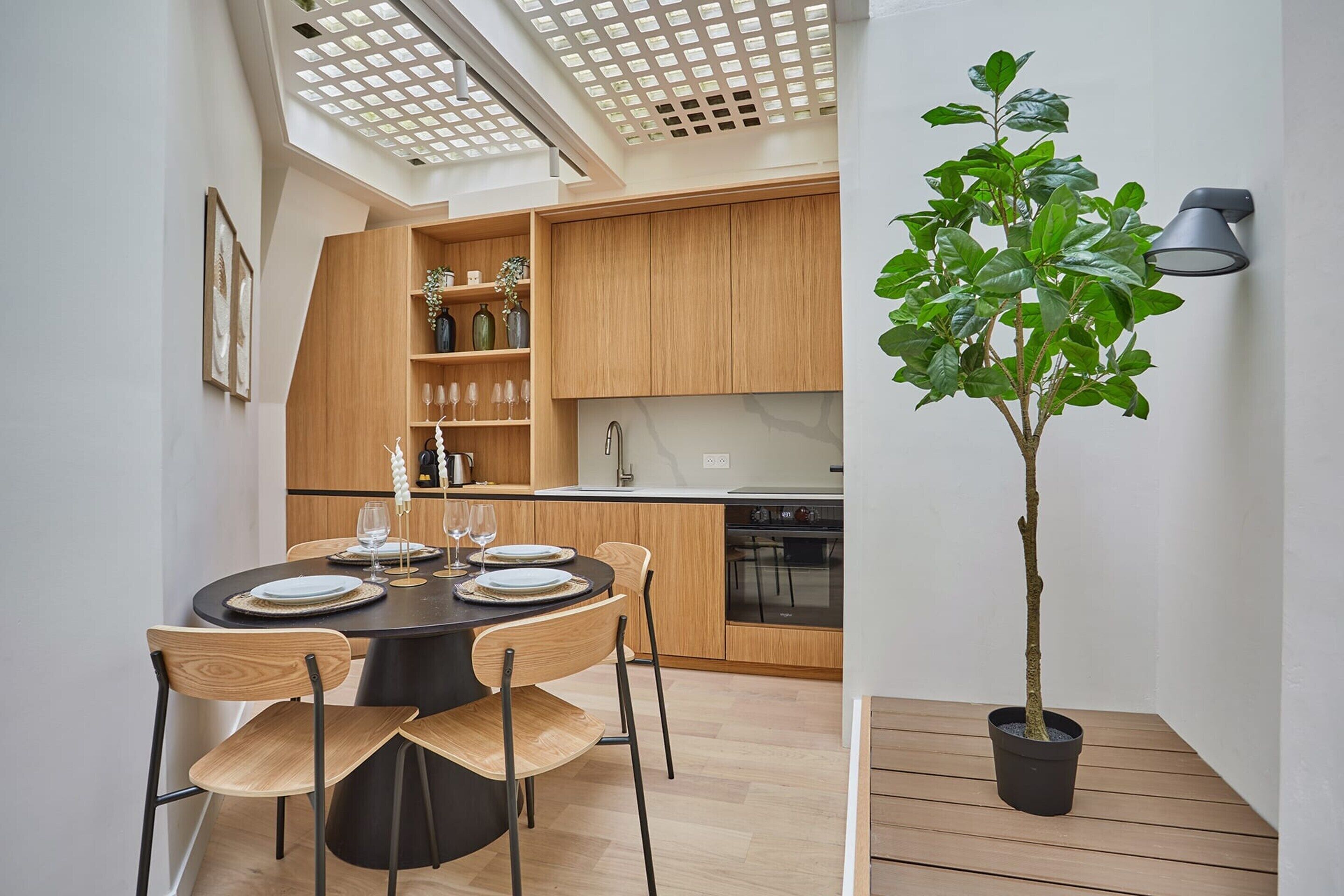 Une cuisine moderne avec des meubles en bois, une table à manger pour quatre personnes et une plante en pot.