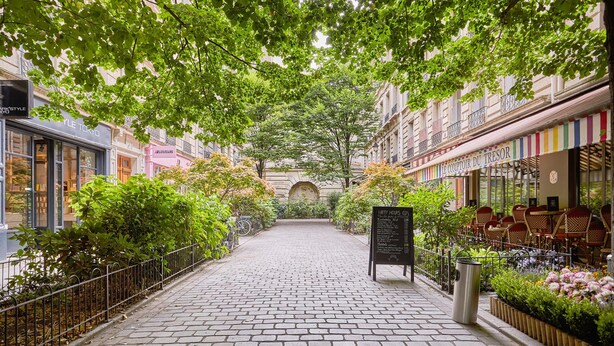 A cobblestone alley with shops on either side, a central archway, and outdoor seating with a menu board. - Sublim Apartment Le Marais Centre de Paris (Paris)
